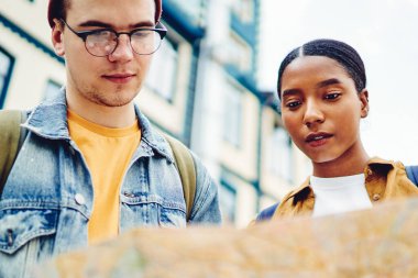 Afrika kökenli Amerikalı genç bir kadın ve Kafkasyalı deneyimli turist şehir merkezinde açık hava haritası okuyorlar. Çeşitli turistlerin görüş açısının altında doğru yönde ve yanlış yönde arama yapıyorlar.