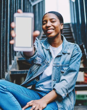Ağ içeriğine yapıştırıcı reklamı yapmak için akıllı telefon kullanan Afrika kökenli Amerikalı bir kadın. Neşeli ve mutlu koyu tenli blogcu cep telefonunu elinde tutuyor.
