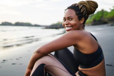 Sahilde sabah eğitim imzatı sırasında gülme ve kameraya bakarak dreads ile Afro amerikan pozitif kadın, mutlu neşeli koyu tenli kadın kıyı şeridinde egzersiz için zaman zevk