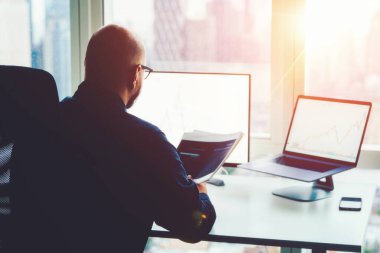 İnsan finansal uzmanının teori ve pratik engelleme teknolojisi üzerine olan arka görüşü. Ofis bilgisayarında elinde borsa istatistikleriyle oturan bir erkek broker. Artan tırnak içinde kazanç