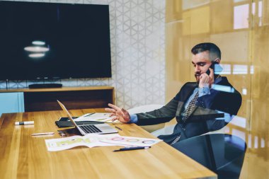 Netbook 'ta çalışan kendine güvenen finans şirketinin sahibi ve yeni projenin iş planını tartışmak için akıllı telefondan arıyor. Takım elbiseli erkek girişimci dijital akıllı telefondan konuşuyor.