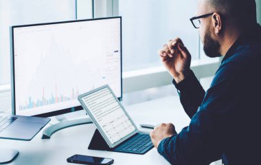 Bilgisayar ve dizüstü bilgisayarlar üzerinde çalışan genç bir çalışan. Ekranda mali bilgi grafikleri var ve ofis masasında oturuyor. Başarılı bir muhasebe işadamı gelir ve araştırma yapıyor. Milenyum çalışması.