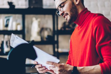 Başarılı gülümseyen, optik göz giysili hippi, rahat dairede kağıt belgelerle uzaktan çalışırken kendini iyi hissediyor. Modern tasarım, pozitif erkek öğrenci üniversite sınavına hazırlanıyor.