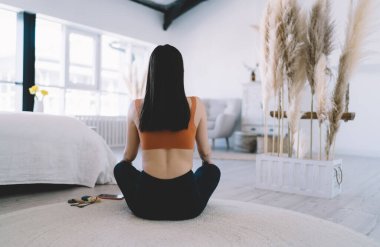Nilüfer çiçeğinde yoga yaparken uzun siyah saçlı ve yerde oturup meditasyon yapan genç bir kadının arka görüntüsü.