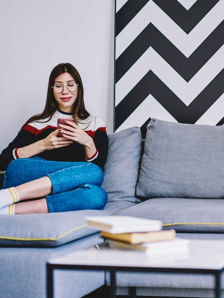 Positive female blogger reading funny message from friend in social network while resting on comfortable couch with husband using modern laptop device for working remotely in stylish home interior