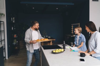 Mutfak tezgahının yanında kruvasanlarla dikilen mutlu adam ve evde ailesiyle kahvaltıya hazırlanıyor.
