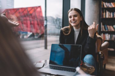 Resmi takım elbiseli neşeli bayan girişimci kahve molası sırasında iş arkadaşınla konuşurken dişlek bir şekilde gülümsüyor.