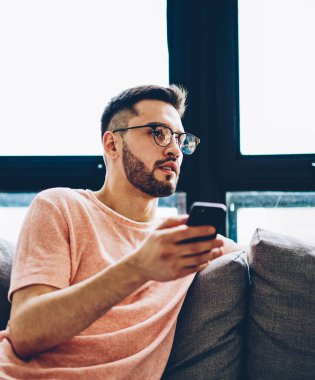 Kafkas sakallı şık gözlüklü adam elinde akıllı telefon cihazıyla apartman koltuğunda dinleniyor ve sosyal ağda yayınlanacak yeni ilginç fikirleri düşünüyor.