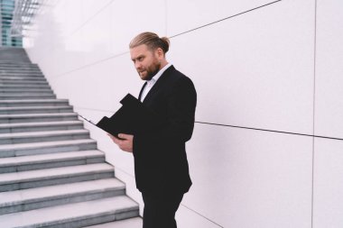 Ciddi bir erkek girişimcinin modern bina merdivenlerinin basamaklarında durup elinde belgeleri tutarken gözlerini kaçırması.