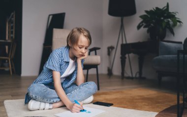 Hafta sonu evdeki oturma odasında bacak bacak üstüne atarak otururken, elinde günlük giysiler ve kağıda karalama yapan tam bir vücut çocuğu.