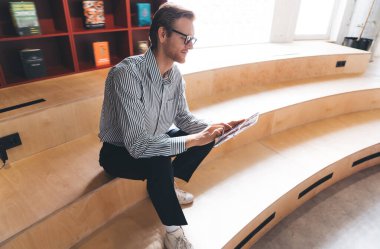 Düşünceli genç iş adamlarının iş kıyafetleri içinde tam boy rahatlama ve dinlenme odasında dinlenme odasında tablet kullanarak yaratıcı tasarım stratejisi üzerinde çalışma