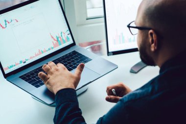 Mali grafikleri inceleyen ve bitcoin fiyatlarının değişkenliğini araştıran konsantre erkeğe yakından bakın. Erkek ofis çalışanı analisti dizüstü bilgisayarda numaralarla çalışıyor.