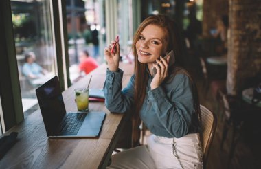 Şık giyinen genç, çekici bir bayan, kameraya bakarak ve akıllı telefonla konuşurken dizüstü bilgisayarını açıyor.