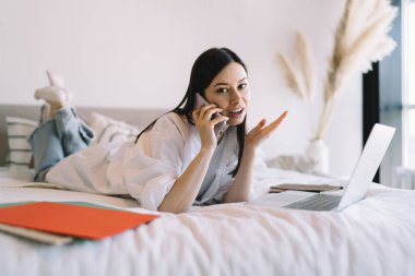 Kendine güveni tam genç bir kadın serbest çalışan. Günlük giysiler içinde. Yatakta uzanmış, cep telefonuyla konuşuyor.