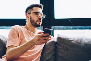 Kafkas sakallı şık gözlüklü adam elinde akıllı telefon cihazıyla apartman koltuğunda dinleniyor ve sosyal ağda yayınlanacak yeni ilginç fikirleri düşünüyor.