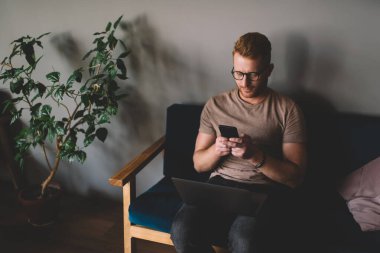 Optik gözlüklü beyaz erkek programcı, bluetooth kullanarak bilgisayar ve akıllı telefon teknolojisiyle cep telefonu üzerinden medya dosyalarını paylaşıyor.