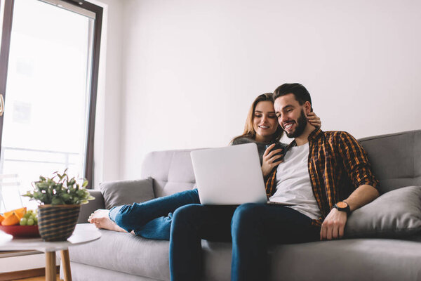 Caucasian couple in love watching positive comedy movie during weekend time in home interior using 4g wireless internet on laptop computer, happy boyfriend and girlfriend browsing video and smile