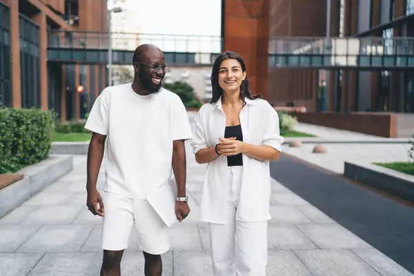 Stock image Happy young multiethnic couple in white outfits smiling and walking together while discussing plans for future on pavement in daytime