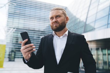 Gündüz vakti gözlüklü ve cep telefonlu modern ofisin önünde duran ciddi erkek girişimcilerin düşük açılı görüntüsü.