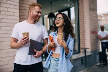 Neşeli kadın ve erkek arkadaşlar gündelik kıyafetleriyle kağıt bardaklarda içki içerler ve kafede yemekten sonra hoş sohbetler ederler.
