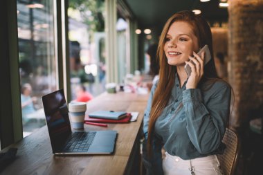 Modern Kafe 'de çevrimiçi işler yaparken yüzünü çeviren ve gülümseyen resmi kıyafetli genç bir bayan serbest yazar.