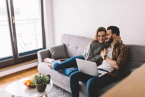 Kafkasyalı çift hafta sonu evde komedi filmi izlerken modern dizüstü bilgisayarda 4G kablosuz internet, mutlu sevgili görüntüsü ve gülümseme videosu kullanıyor.