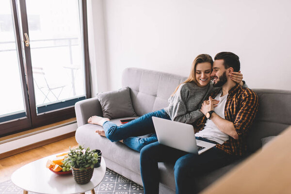 Caucasian couple in love watching positive comedy movie during weekend in home interior using 4g wireless internet on modern laptop computer, happy boyfriend and girlfriend browsing video and smile