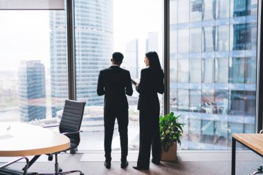 Tanımlanamayan iş arkadaşlarının resmi giysiler içinde masanın yanında sandalyeyle durmaları ve iş stratejilerini çağdaş iş yerlerinde pencerenin yanında tartışmaları