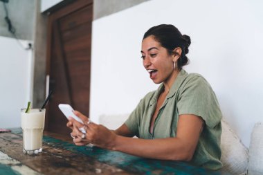 Serinletici içkisi olan genç bayan ve güzel haberler hakkında heyecanla telefon ekranına bakıyor.