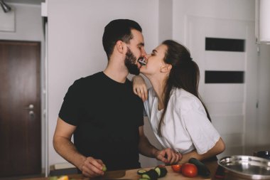 Mutlu erkek ve kadın eşler, kendi evlerinde birlikte yemek pişirmek için boş vakitlerin tadını çıkarıyorlar. Kafkasyalı karı koca, tezgahta kahvaltı hazırlıyorlar. Taze salatalık.