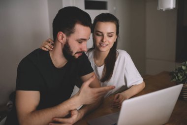 Yüksek açılı rahat elbiseli romantik bir çift evde oturmuş netbook 'ta konsantrasyonlu ilginç videolar izliyorlar.