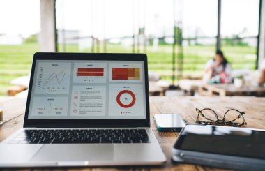 Modern netbook, akıllı telefon ve tabletin yanına yerleştirilmiş grafikler ve grafikler ile güncel kafedeki ahşap masaya yerleştirilmiştir.