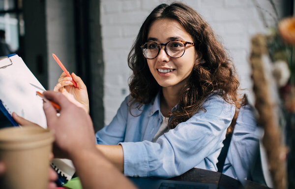 Кавказские коллеги-мужчины и женщины, анализирующие информационные заметки во время совместной встречи в местном кафе, молодые деловые партнеры сотрудничают по планированию организации - обсуждают идеи в помещении