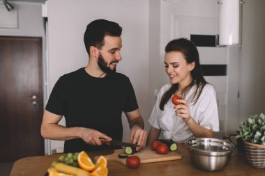 Kaygısız eş hafta sonu birlikte yemek pişirmenin keyfini çıkarıyor ve ev mutfağında gülümsüyor, mutlu erkek ve dişi 20 'li yaşlarda domates ve salatalık salatası hazırlarken iletişim kuruyor.