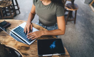 Kafe 'de proje bilgilerini ararken ahşap masada elinde aletlerle oturup dizüstü bilgisayarını karıştıran tanınmayan serbest çalışan yüksek açılı kadın.