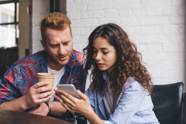 Sosyal medya ağlarında web sayfası için içerik planlarını tartışan genç arkadaşlar cep telefonu teknolojisini birlikte kullanırken, milenyum hipster erkekleri kahve dükkanında cep telefonlarını kablosuz olarak tarıyorlar.