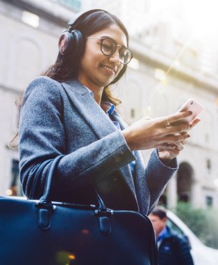 Gülümseyen Hintli kadın, şehir caddesinde durup işten sonra dinlenirken kulaklıkla müzik dinliyor. Genç bir kadın kulaklıkla müzik listesinden hoşlanıyor. Sosyal ağdaki içeriği izlemek, milenyum