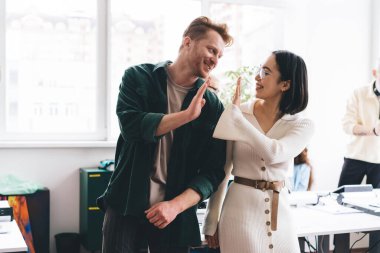 Pozitif, genç, çok ırklı erkek ve kadın meslektaşlar ışık odasında pencerenin yanında durup gülerek ve tezahürat yaparken birbirlerine bakıyorlar.