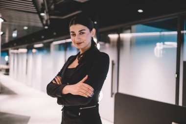 Kollarını kavuşturup gülümseyen ve modern ofiste kameraya bakan kendine güvenen genç, etnik kadın yöneticiler.