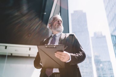 Resmi giysiler içinde, elinde kalem gözlükleriyle cam duvarın yanında duran ve modern ofise gözlerini çeviren son sınıf erkek girişimcilerden.