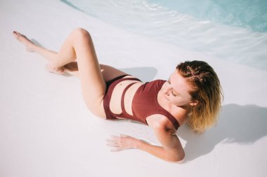 Mavi havuz suyunda poz verirken mayo giymiş genç ve zayıf bir kadının yukarıdan görünüşü.