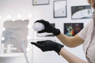 Meçhul kadın uzman siyah lateks eldivenler modern güzellik kliniğinde yüz temizleme için pamuk yastığa jöle döküyor.