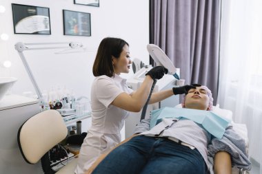 Modern klinikte güzellik prosedürü sırasında YAG lazeri kullanarak hastaların yüzüne saç aldırma konusunda uzman.