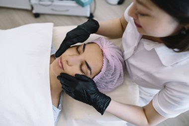 Güzellik merkezindeki masada uzanmış, gözleri kapalı, sakince masaj yapan kadın müşterinin yüksek açılı ürünü.