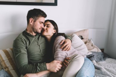 Gündelik giysiler içinde genç bir çift. Yatakta birlikte vakit geçirirken kapalı gözlerle sarılıyorlar. Aşklarını ifade ediyorlar.