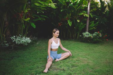 Gündüz vakti ısınırken ve yeşil çimlere bakarken çıplak ayaklı, esnek bacaklı, sakin, genç bir kadın vücudu.