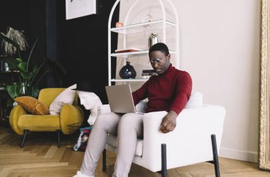 Ciddi Afrika kökenli Amerikalı erkek metin yazarı. Evdeki rahat koltukta oturup internet üzerinde çalışırken makale yazıyor ve yayın yapıyor.