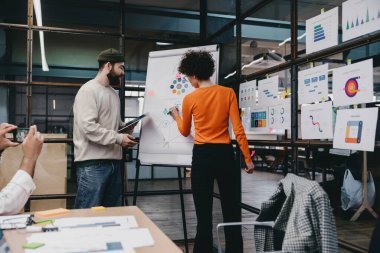 Ofisteki projenin detaylarını analiz ederken ve tartışırken, çizelgelerle ve şemalarla yan yana duran sıradan giyinen erkek arkadaşlarıyla yüzsüz bir kadının arka plan görüntüsü.