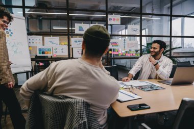 Modern ofisteki projenin detaylarını tartışırken ve beyin fırtınası yaparken gündelik kıyafetlerini giymiş bir grup pozitif genç bilgisayar ve tabletle masada oturuyor.