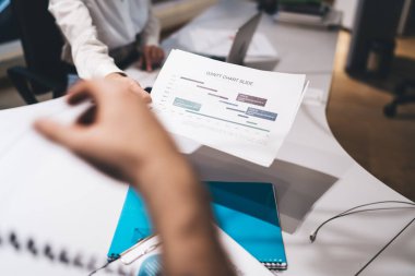 İş profesyonelleri proje zaman çizelgelerini gösteren çizelgeyi sunar. Bulanık arka plan, proje yönetiminde planlama ve yürütme üzerine yoğunlaşan bir ofis ortamını gösteriyor